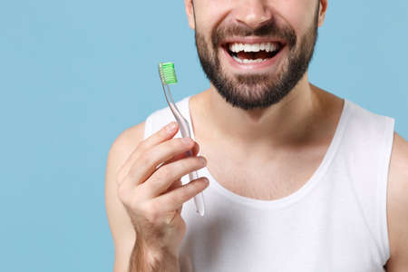 Close up cropped bearded young man in white shirt hold choice electric brushes isolated on blue pastel background studio portrait. Skin care healthcare cosmetic procedures concept Mock up copy space.の写真素材