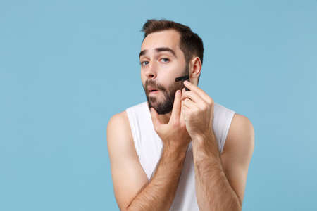 Bearded man 20s years old in white shirt hold one-off disposable plastic razor isolated on blue pastel background studio portrait. Skin care healthcare cosmetic procedures concept. Mock up copy space.の写真素材