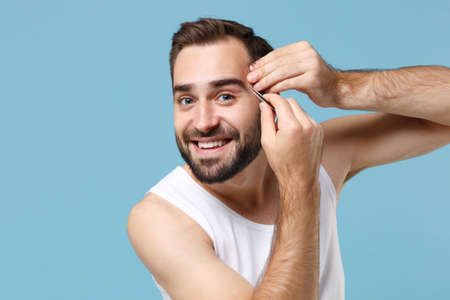 Close up bearded young man 20s years old in white shirt hold in hand tweezers isolated on blue pastel background, studio portrait. Skin care healthcare cosmetic procedures concept. Mock up copy space.の写真素材