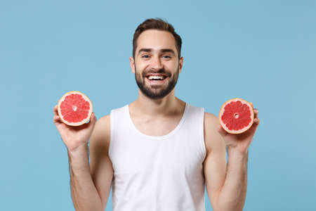 Bearded young man 20s years old in white shirt hold in hand half of grapefruit isolated on blue pastel background, studio portrait. Skin care healthcare cosmetic procedures concept. Mock up copy spaceの写真素材