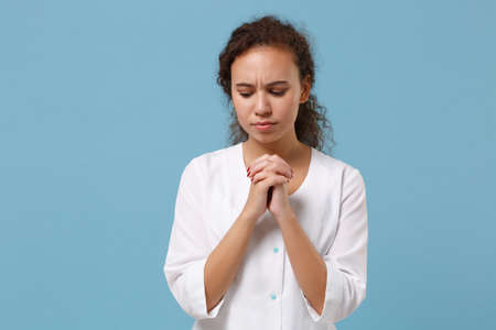 Pensive african american doctor woman isolated on blue background. Female doctor in white medical...