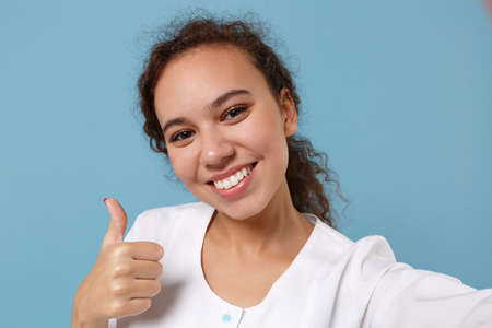 African american doctor woman isolated on blue background. Doctor in medical gown doing selfie shot...