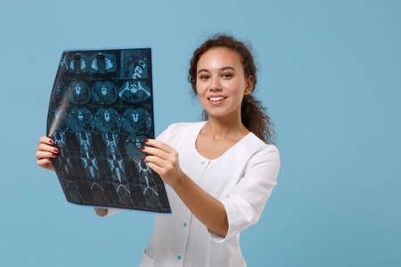 Smiling african american doctor woman in medical gown holding x-ray the brain by radiographic image ct scan mri isolated on blue background. Healthcare personnel medicine concept. Mock up copy space.の写真素材
