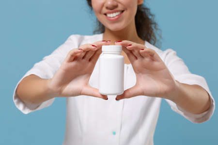 Cropped image of african american female doctor woman in medical gown holding tablets, aspirin pills in bottle isolated on blue background. Healthcare personnel medicine concept. Mock up copy space.の写真素材