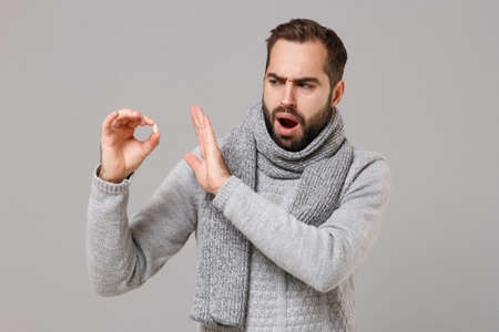 Young man in gray sweater, scarf isolated on grey background. Healthy lifestyle ill sick disease treatment cold season concept. Mock up copy space. Showing stop gesture with palm to medication tablet.の写真素材