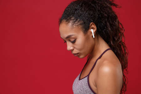 Side view of young african american sports fitness woman in sportswear working out isolated on red...