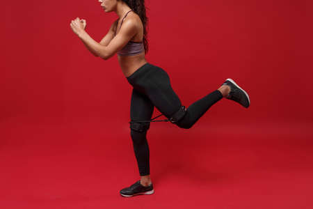Cropped image side view of african american sports fitness woman in sportswear working out isolated on red background in studio. Sport exercises healthy concept. Doing exercises with elastic band.の写真素材
