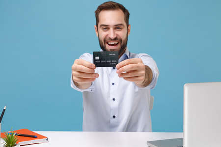 Cheerful young bearded man in light shirt sit and work at white desk with pc laptop isolated on...