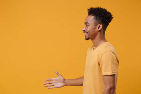 Side view of young african american guy in casual t-shirt posing isolated on yellow orange wall...