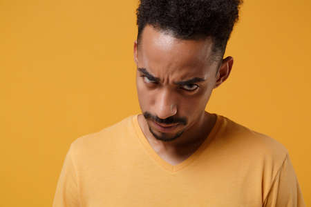 Close up of displeased young african american guy in casual t-shirt posing isolated on yellow orange background studio portrait. People emotion lifestyle concept. Mock up copy space. Looking camera.の写真素材