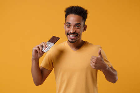 Smling young african american guy in casual t-shirt posing isolated on yellow orange background...