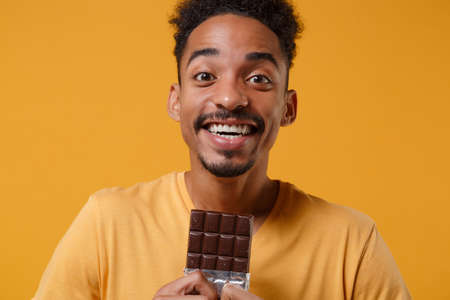 Excited young african american guy in casual t-shirt posing isolated on yellow orange background...