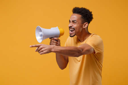 Angry young african american guy in casual t-shirt posing isolated on yellow orange background in...