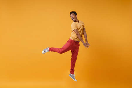 Cheerful young african american guy in casual clothes posing isolated on yellow orange background studio portrait. People sincere emotions lifestyle concept. Mock up copy space. Jumping looking aside.の写真素材
