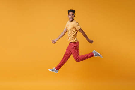 Side view of excited young african american guy in casual clothes posing isolated on yellow orange background, studio portrait. People lifestyle concept. Mock up copy space. Jumping, looking camera.の写真素材