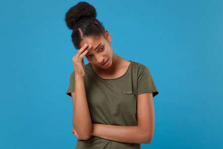 Preoccupied young african american woman girl in casual t-shirt posing isolated on bright blue wall background in studio. People lifestyle concept. Mock up copy space. Looking aside, put hand on head.の写真素材