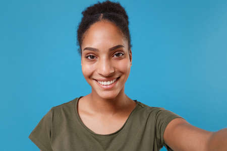 Close up of smiling young african american woman girl in casual t-shirt posing isolated on blue...