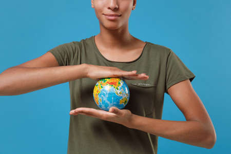 Cropped image of young african american woman girl in casual t-shirt posing isolated on blue background studio portrait. People emotions lifestyle concept. Mock up copy space. Hold Earth world globe.の写真素材