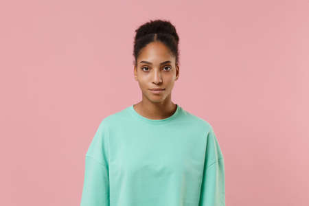 Beautiful young african american woman girl in green sweatshirt posing isolated on pastel pink background studio portrait. People sincere emotion lifestyle concept. Mock up copy space. Looking camera.の写真素材