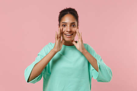 Cheerful young african american girl in green sweatshirt posing isolated on pastel pink background...