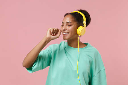 Funny young african american girl in green sweatshirt isolated on pastel pink wall background....