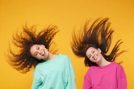 Two cheerful women friends european african american girls in pink green clothes posing isolated on...