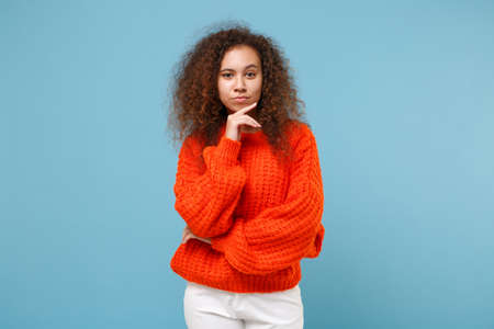 Smiling young african american girl in casual orange knitted clothes isolated on pastel blue background studio portrait. People sincere emotions, lifestyle concept. Mock up copy space. Looking cameraの写真素材