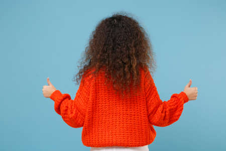 Back rear view of young african american girl in casual orange knitted clothes isolated on pastel...