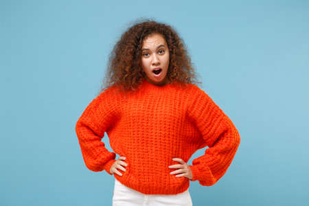 Shocked irritated young african american girl in casual orange knitted clothes isolated on pastel blue background. People lifestyle concept. Mock up copy space. Standing with arms akimbo on waist.の写真素材