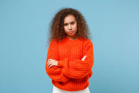 Dissatisfied young african american girl in casual orange knitted clothes isolated on pastel blue...