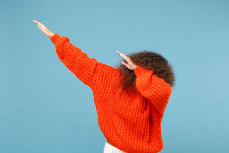 Young african american girl in casual orange knitted clothes isolated on pastel blue wall background studio portrait. People emotions lifestyle concept. Mock up copy space. Showing DAB dance gesture.の写真素材