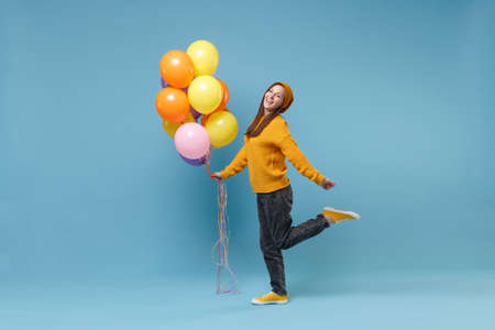 Funny young woman girl in sweater hat posing isolated on blue background studio portrait. Birthday holiday party people emotions concept. Mock up copy space. Celebrating holding colorful air balloons.の写真素材