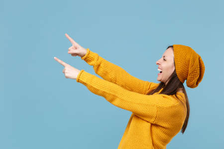 Laughing young woman girl in yellow sweater and hat posing isolated on blue background studio portrait. People sincere emotions lifestyle concept. Mock up copy space. Pointing index fingers aside.の写真素材