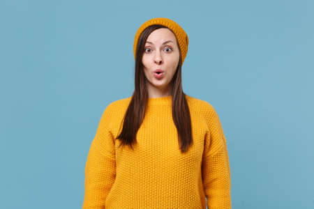 Shocked young brunette woman girl in yellow sweater and hat posing isolated on blue wall background studio portrait. People sincere emotions lifestyle concept. Mock up copy space. Keeping mouth open.の写真素材
