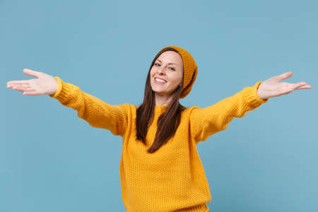 Smiling young brunette woman in yellow sweater hat posing isolated on blue background studio...