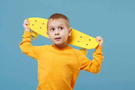 Little cute kid boy 4-5 years old wearing yellow clothes hold in hand skate board isolated on pastel blue wall background, children studio portrait. People sincere emotions childhood lifestyle conceptの写真素材