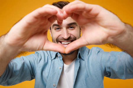 Smiling young bearded man in casual blue shirt posing isolated on yellow orange background in...