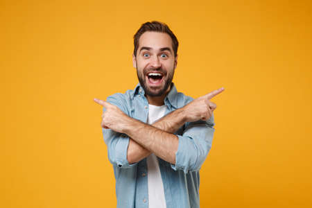 Excited young bearded man in casual blue shirt posing isolated on yellow orange background in...