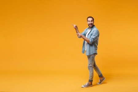 Excited young bearded man in casual blue shirt posing isolated on yellow orange background studio portrait. People sincere emotions lifestyle concept. Mock up copy space. Pointing index fingers aside.の写真素材