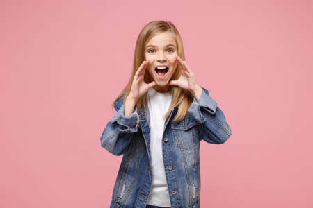 Cheerful little kid girl 12-13 years old in denim jacket isolated on pastel pink background children portrait. Childhood lifestyle concept. Mock up copy space. Screaming with hands gesture near mouth.の写真素材