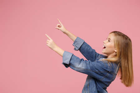 Side view of funny little kid girl 12-13 years old in denim jacket isolated on pastel pink background children portrait. Childhood lifestyle concept. Mock up copy space. Point index fingers aside up.の写真素材