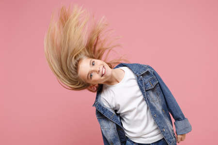 Cheerful little blonde kid girl 12-13 years old in denim jacket isolated on pastel pink wall background children portrait. Childhood lifestyle concept. Mock up copy space. Having fun with flying hair.の写真素材