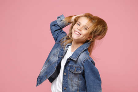 Smiling little blonde kid girl 12-13 years old in denim jacket isolated on pastel pink background...