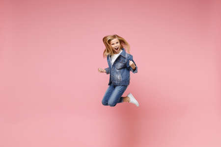 Screaming little blonde kid girl 12-13 years old in denim jacket isolated on pastel pink background...