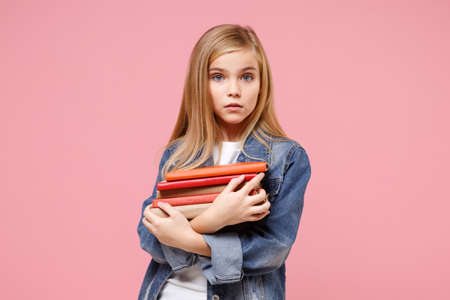 Beautiful little blonde kid girl 12-13 years old in denim jacket isolated on pastel pink background children studio portrait. Childhood lifestyle concept. Mock up copy space. Holding books, notebooks.の写真素材