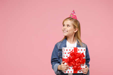 Smiling little kid girl 12-13 years old in birthday hat isolated on pastel pink wall background....