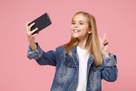 Pretty little kid girl 12-13 years old in denim jacket isolated on pastel pink wall background....