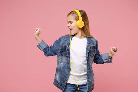 Funny little kid girl 12-13 years old in denim jacket isolated on pastel pink background in studio. Childhood lifestyle concept. Mock up copy space. Listen music with headphones dancing sing song.の写真素材
