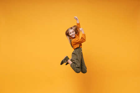 Smiling little kid girl 12-13 years old in turtleneck, jumpsuit isolated on orange yellow background...