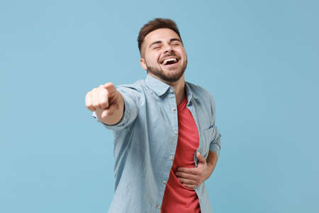 Laughing young bearded guy in casual shirt posing isolated on pastel blue background studio...